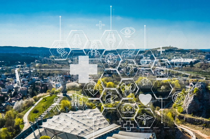 Zdjęcie panoramy Kielc z amfiteatrem na pierwszym planie a na tym infografiki związane ze zdrowiem jak strzykawka, serce, ekg